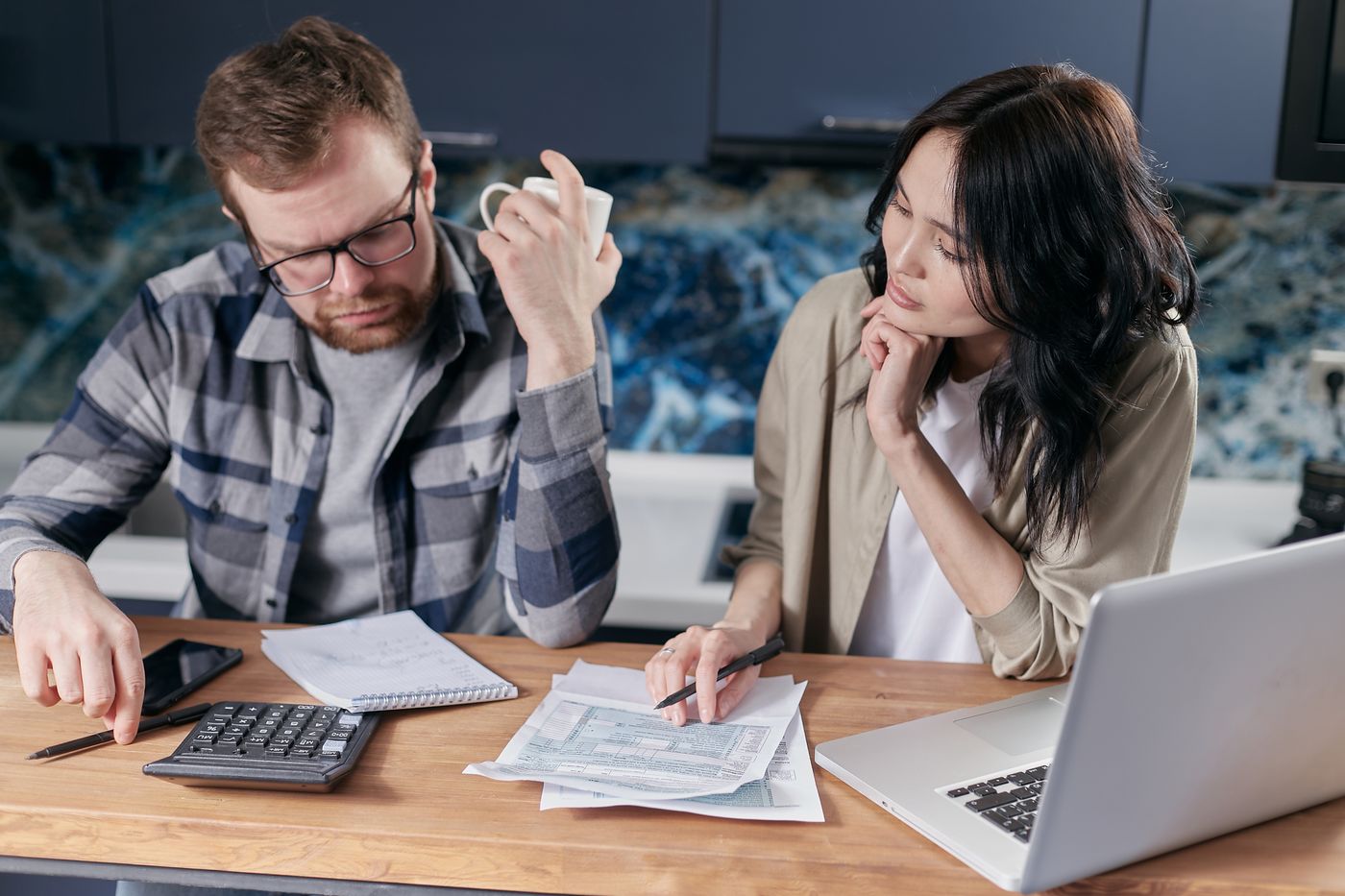 A freelancer couple at the kitchen table going over tax paperwork with a calculator